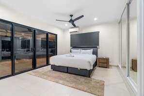 A modern bedroom with a bed, a ceiling fan, a nightstand, and a sliding glass door leading to a balcony.