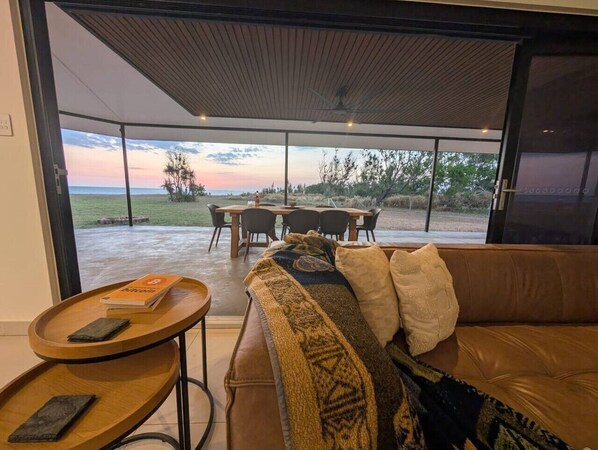 A modern living room with a large window, a sofa, a table, and a dining area.