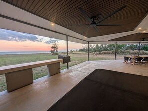 Un espace extérieur aménagé en terrasse, avec un banc, une table et une vue sur l’océan au coucher du soleil.