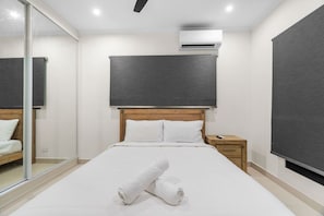 A hotel room with a bed, a nightstand, a mirror, and an air conditioning unit.