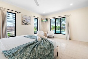 Habitación de hotel con cama, dos sillones, televisor y ventanas amplias con cortinas.