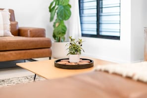 A living room with a brown leather sofa, a small potted plant on a round wooden tray, and a window with blinds.