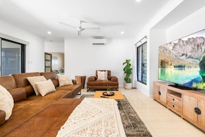 A modern living room with a brown leather sofa, a wooden coffee table, a large flat-screen TV, and a ceiling fan.