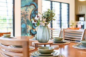 Ein Essbereich mit Tisch für zwei Personen, eine Vase mit Blumen, Holzstühle und Blick in die Küche.