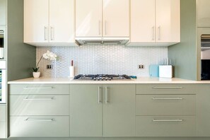 Una cocina con armarios de colores claros, un protector contra salpicaduras de azulejos y una estufa a gas.
