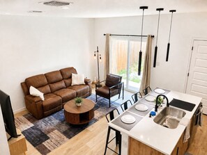 A modern kitchen with a dining area, a brown leather sofa, and a small round table with a plant.