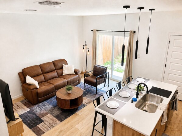 A modern kitchen with a dining area, a brown leather sofa, and a small round table with a plant.
