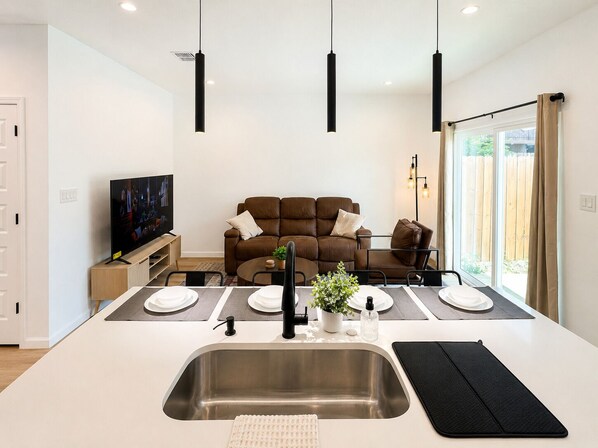 A modern kitchen with a central island, a dining area, and a living room with a sofa.