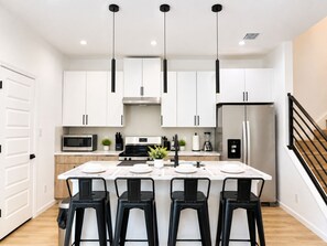 A modern kitchen with white cabinets, a central island with bar stools, a stainless steel refrigerator, and a microwave.
