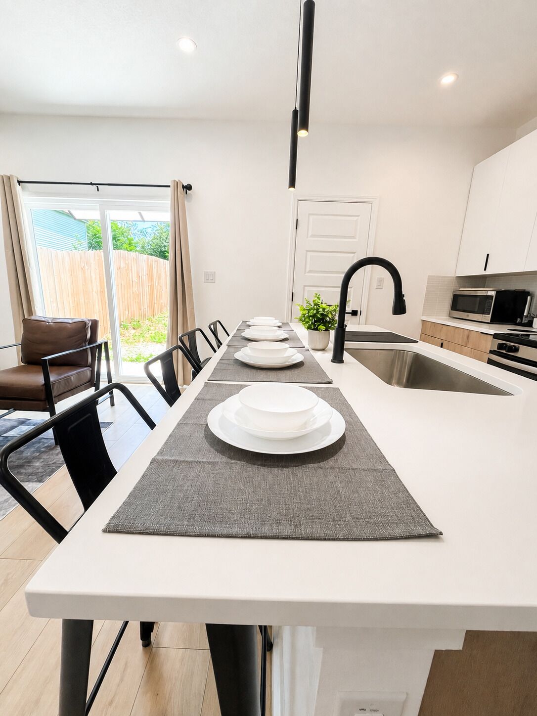 A modern kitchen with a central island, a dining area with chairs, and a sliding glass door leading to a patio.