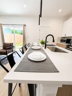 A modern kitchen with a central island, a dining area with chairs, and a sliding glass door leading to a patio.