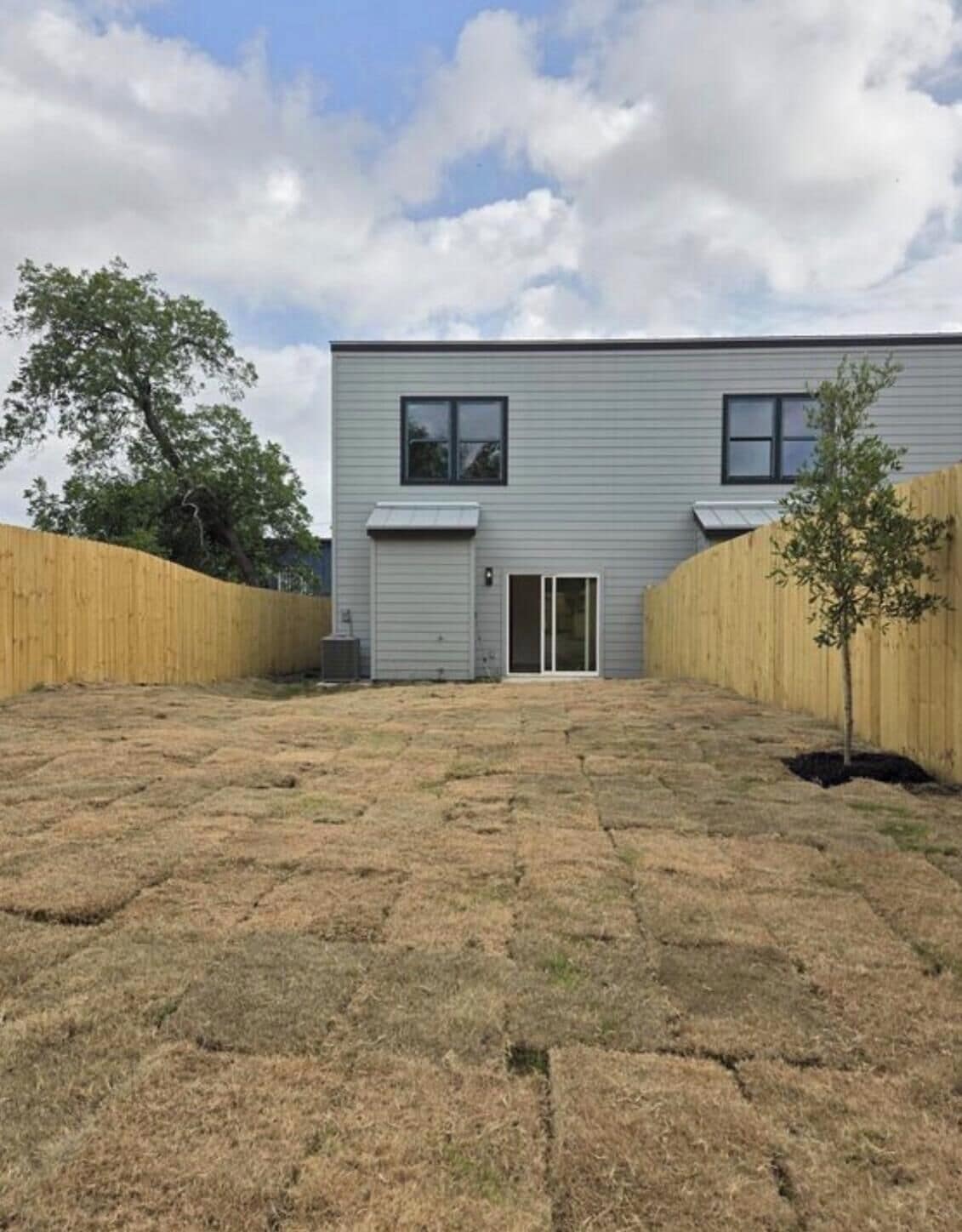 A two-story building with a flat roof, a front door, and a small tree in the yard.