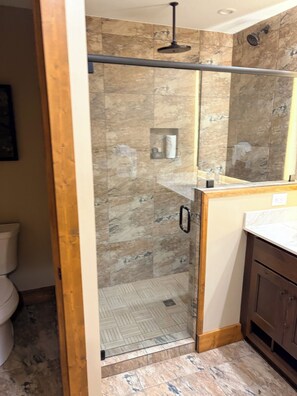Un bagno con cabina doccia in vetro, pareti in marmo e mobile lavabo in legno.