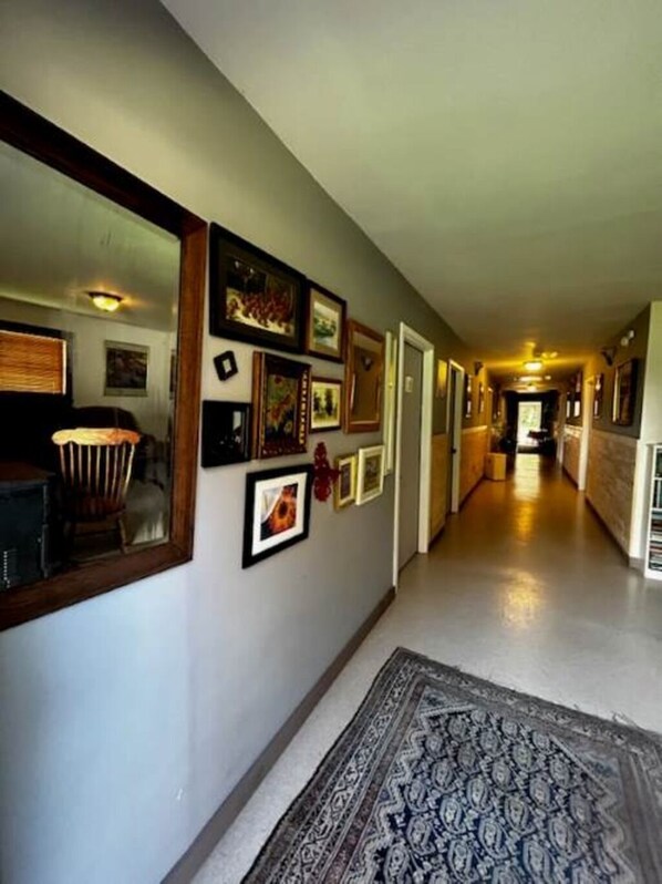 A hallway with framed pictures on the walls, a rug on the floor, and a door at the end.