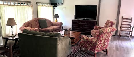 Una sala de estar con sofá, sillón, mesa de centro y televisor de pantalla plana.