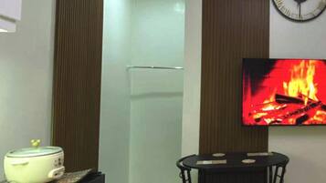 Un espacio habitable compacto con kitchenette, zona de comedor, televisor de pantalla plana y lámpara en el techo.