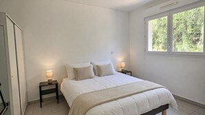 Un dormitorio con cama, dos mesitas de noche con lámparas, una ventana y vista a zonas verdes.
