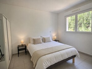 Ein Schlafzimmer mit einem Bett, zwei Nachttischen mit Lampen, einem Fenster und Blick ins Grüne.
