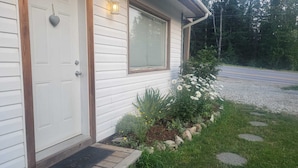 A house with a white exterior, a front door, a window with blinds, and a garden with flowers and plants.