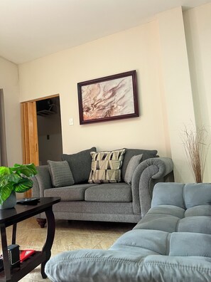 A living room with a grey sofa, a coffee table, a framed abstract painting, and a potted plant. - Island Escape Wonderful 2-bedroom apartment with AC in charming Kelly Village (Kelly Village)