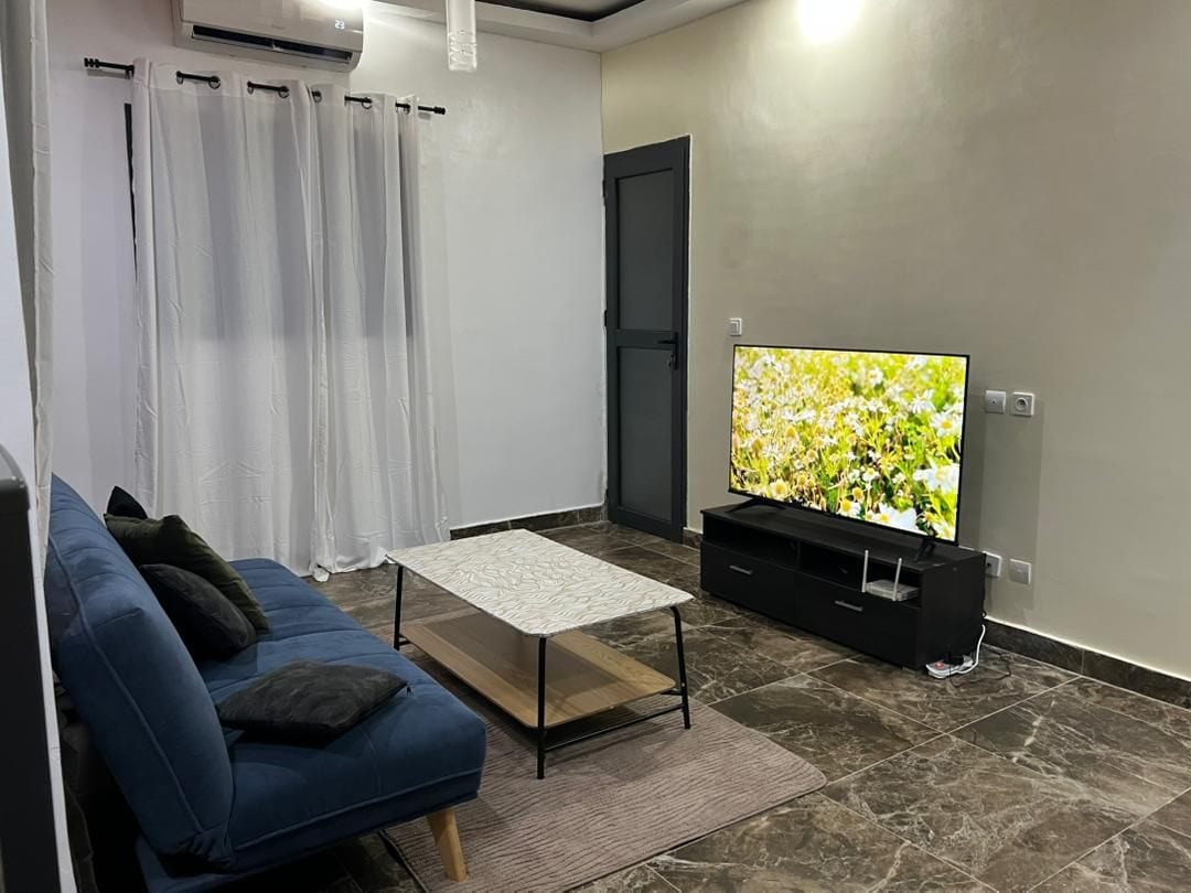 Een woonkamer met een blauwe bank, een salontafel, een flatscreen televisie en een deur.