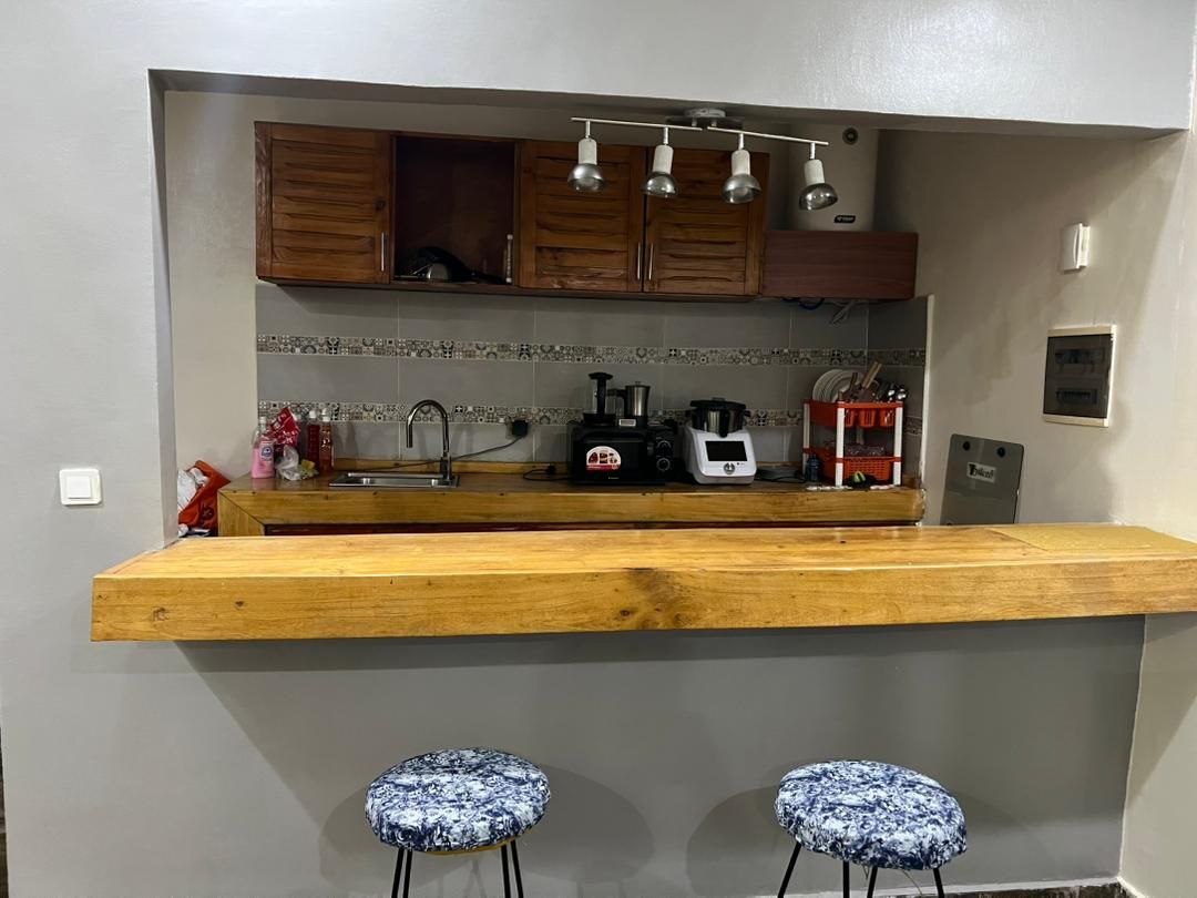 A kitchen with wooden cabinets, a countertop, a sink, and two stools.