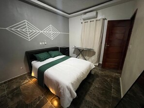 Ein Schlafzimmer mit einem Bett, einem Bügelbrett, einer Wandklimaanlage und einer Tür.
