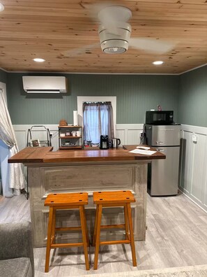 Eine kleine Küche mit Holzboden, einem eingebauten Kühlschrank, einer Mikrowelle und einer Kaffeemaschine auf der Arbeitsfläche.