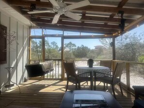 Un espace extérieur abrité, équipé d’une table et de chaises, d’un ventilateur de plafond et offrant une vue sur le paysage environnant.