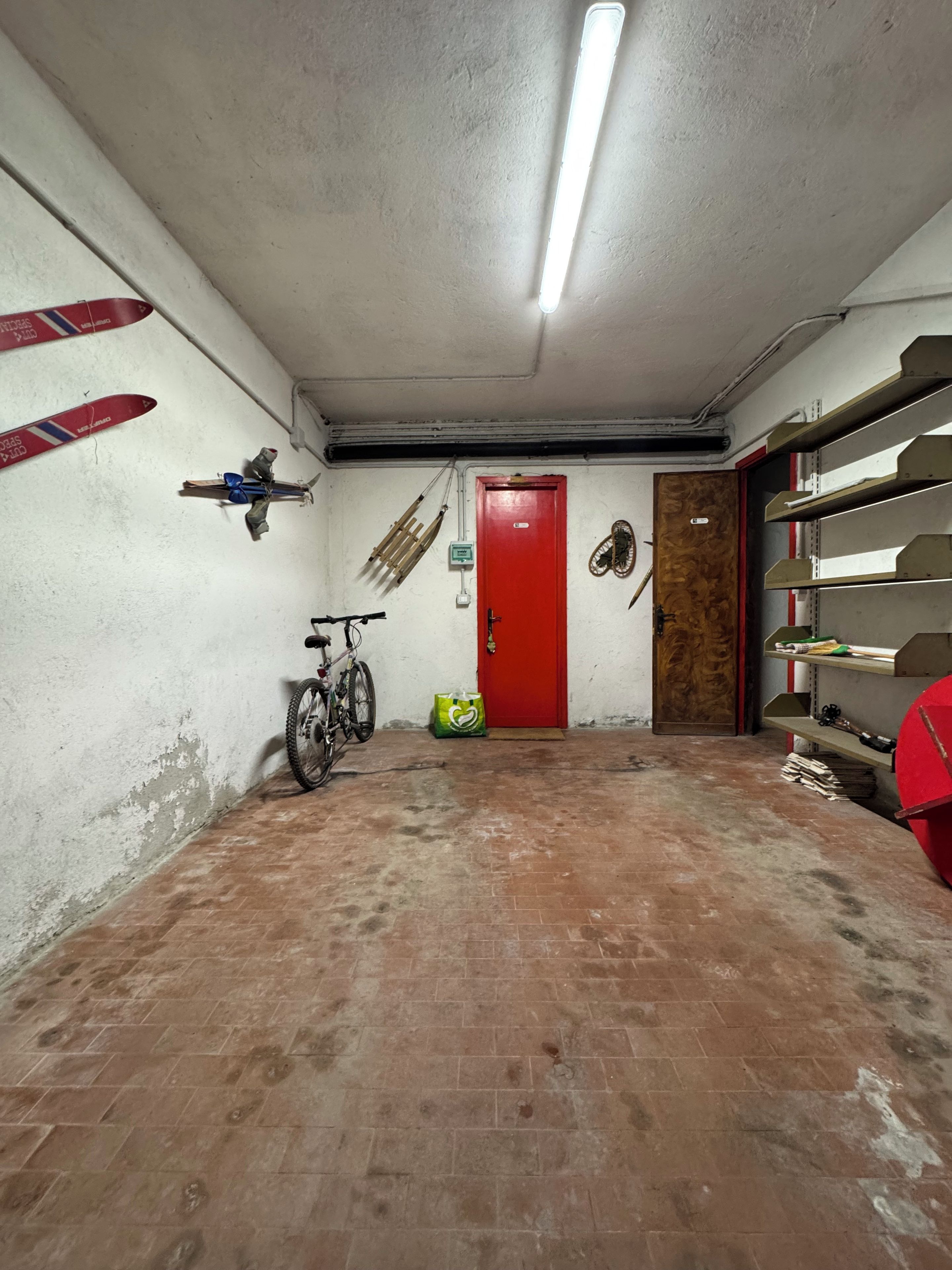 Eine Garage mit einer roten Tür, einem Fahrrad und Regalen voller Werkzeug.