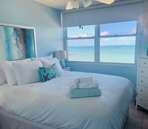 A bedroom with a large bed, a view of the ocean, and a painting on the wall. - Peaches Pura Vida ~ Signature Oceanfront Luxury (Carolina)