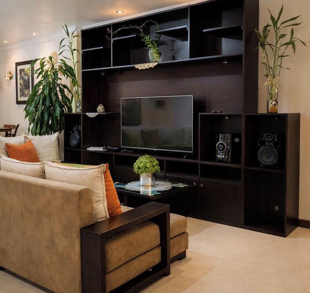 A living room with a sofa, a coffee table, a flat-screen TV, and a dark entertainment unit with speakers and decorative items.