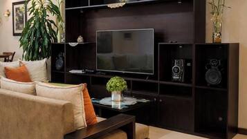A living room with a sofa, a coffee table, a flat-screen TV, and a dark entertainment unit with speakers and decorative items.