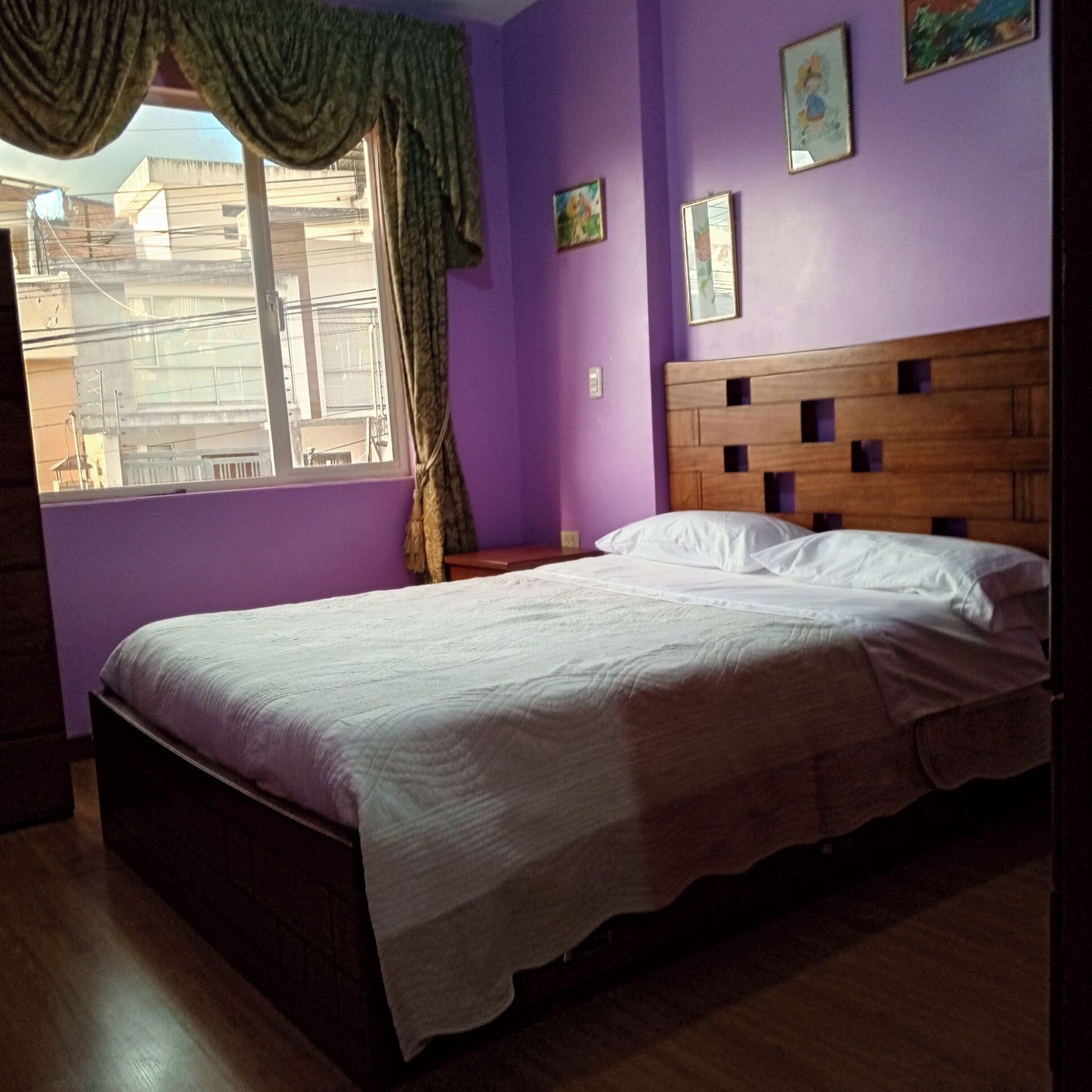 A bedroom with a bed, a window with curtains, and a purple wall.