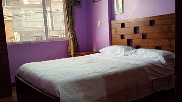 A bedroom with a bed, a window with curtains, and a purple wall.