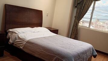 A bedroom with a wooden bed, a nightstand, a framed picture on the wall, and a window with curtains.