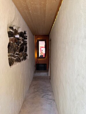 A narrow hallway with a stone wall on the left, a wooden ceiling, and a door at the end. - A home you'll want to stay in, with a terrace overlooking the mountains and the village (Castelo de Vide)