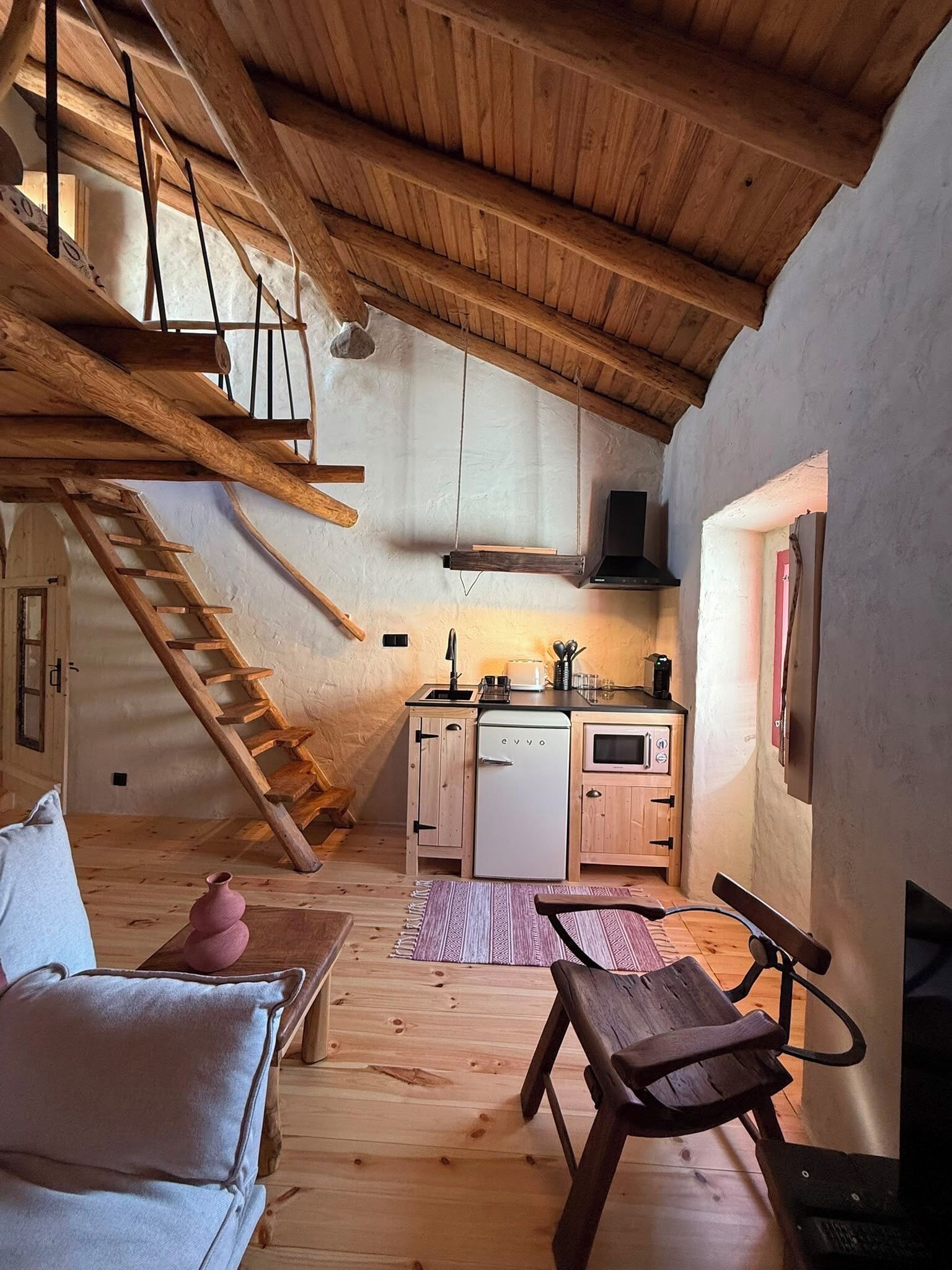 A rustic loft bedroom with a loft bed, a small kitchenette, and a cozy seating area.