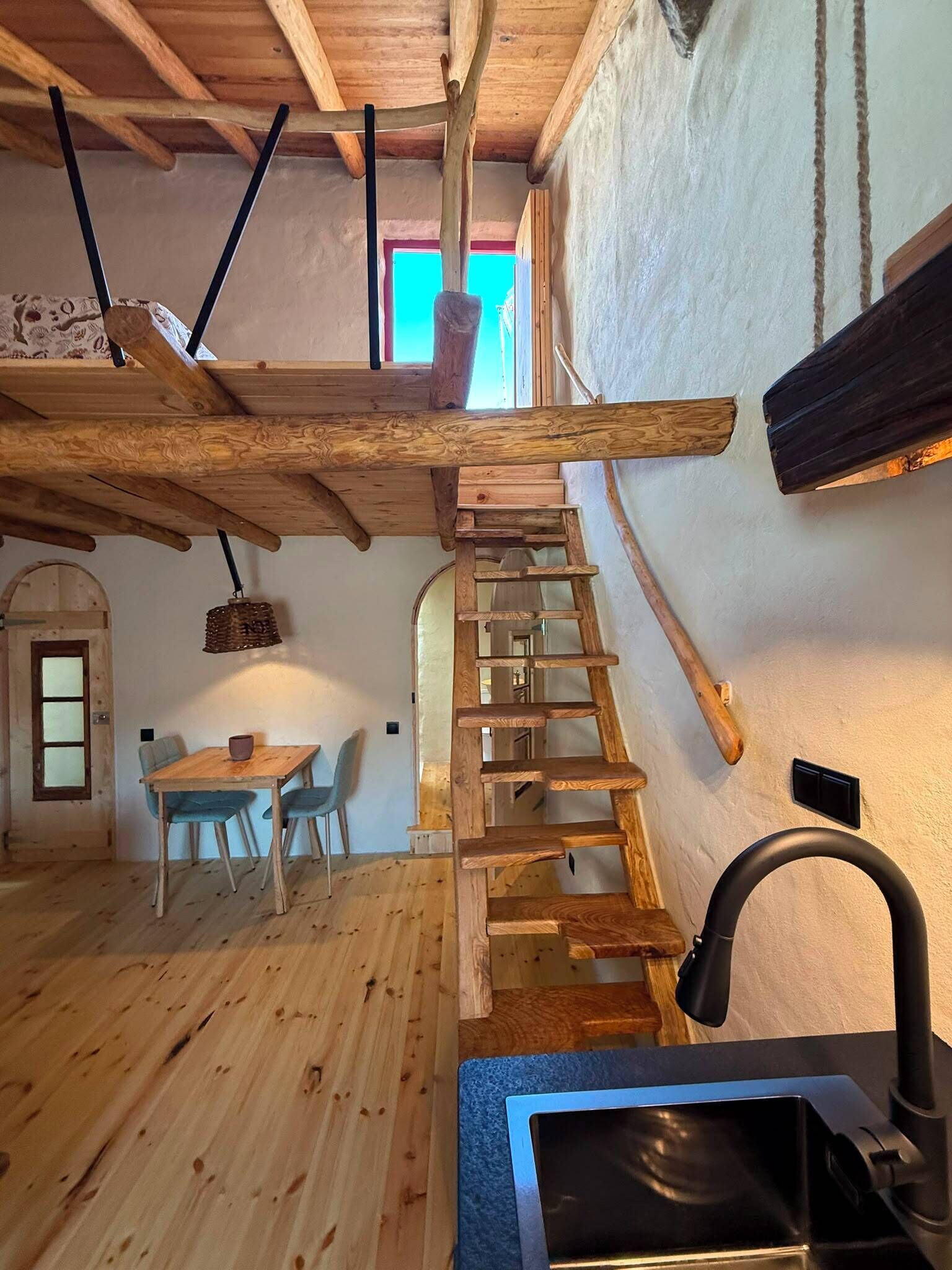 A wooden interior with a staircase, a dining area, and a view of the outside.