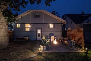 Kaksikerroksinen talo, jossa on patio ja ulkotila, jossa on istuimia ja nuotiopaikka.