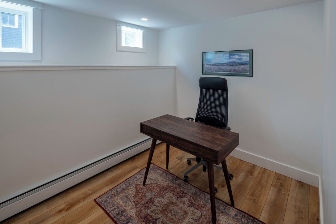 A room with a wooden desk, a chair, a rug, a picture on the wall, and a window.