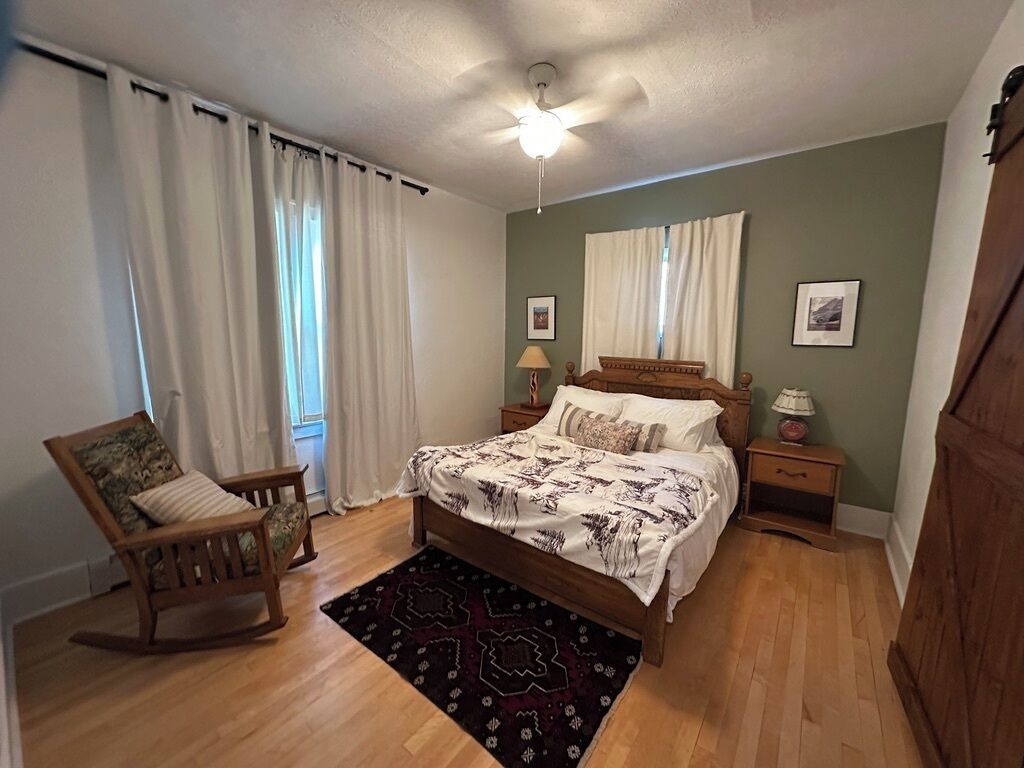 Ein Schlafzimmer mit einem Bett, einem Schaukelstuhl, einem Nachttisch mit Lampe und einem Deckenventilator.