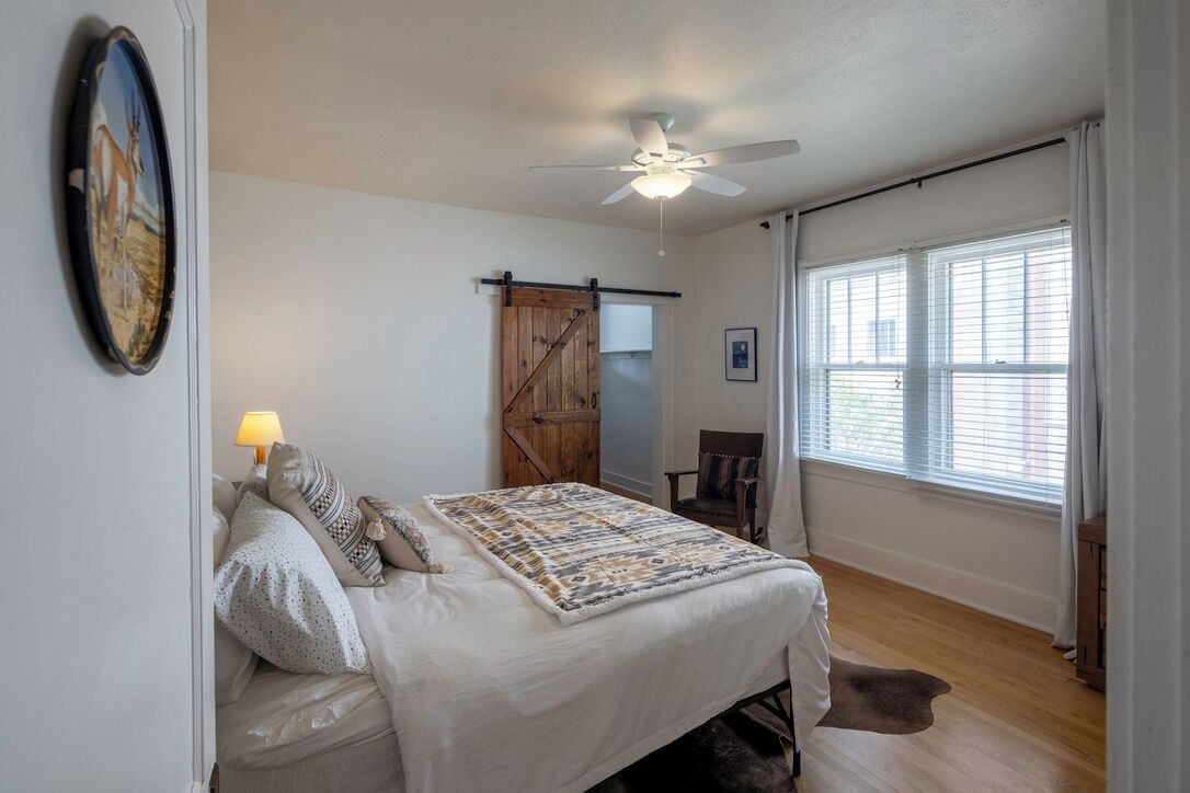 Ein Schlafzimmer mit einem Bett, einem Deckenventilator, einem Fenster mit Vorhängen und einer Holztür.