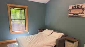 A bedroom with a bed, a window, a nightstand, a cabinet, and a wall-mounted picture.