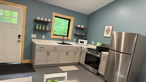 A modern kitchen with grey cabinets, a stainless steel refrigerator, a microwave, and a stove. There is a window above the sink, and a plant on the table.