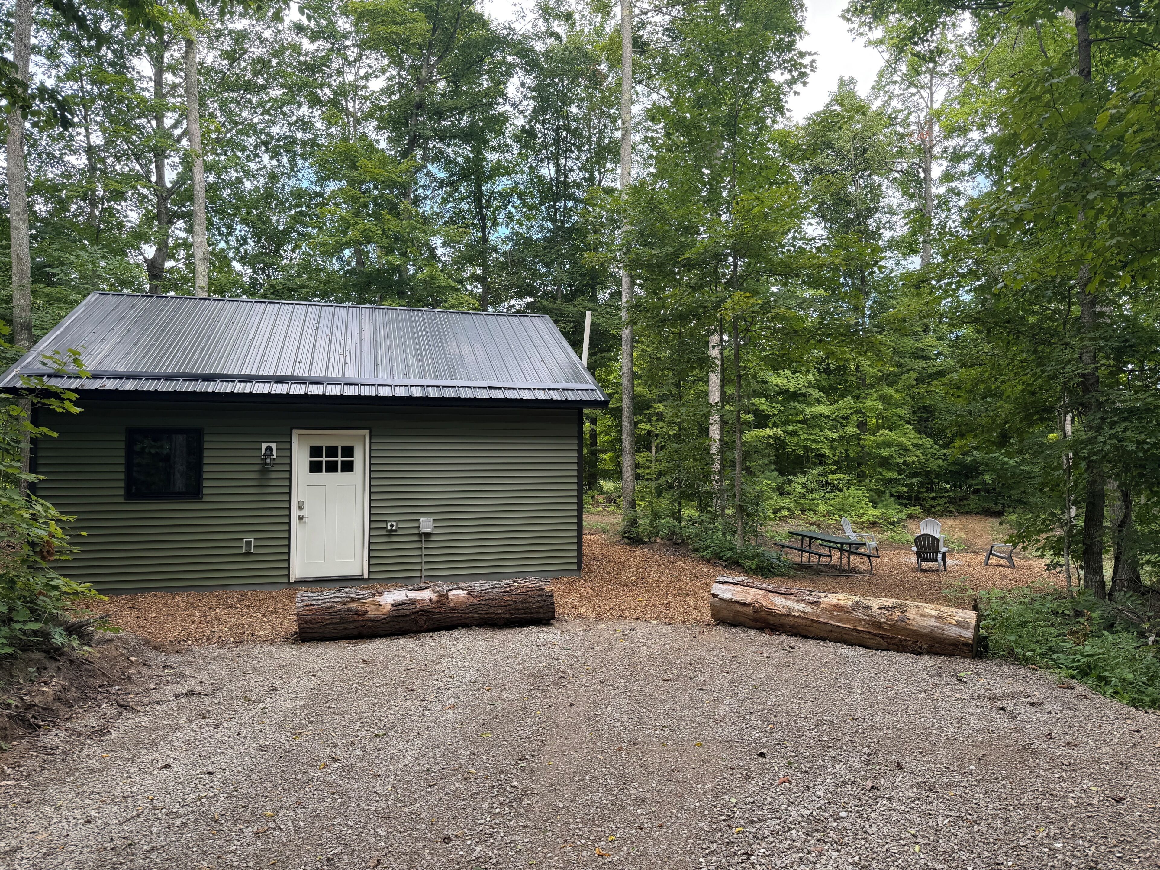 Une petite cabane avec une allée en gravier, entourée d’une forêt dense.