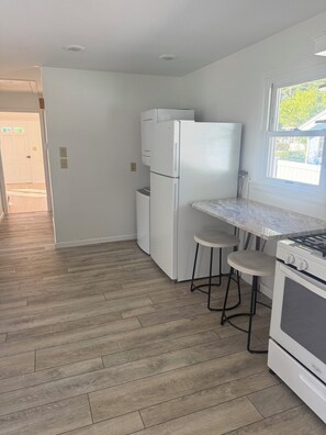 A kitchen with a white refrigerator, a stove, and two bar stools. - Adorable 2-bedroom Seasonal Rental in Milford Beach Neighborhood (Milford)