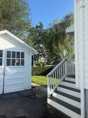 A white garage with a door, a small covered porch with a railing, and a concrete driveway. - Adorable 2-bedroom Seasonal Rental in Milford Beach Neighborhood (Milford)