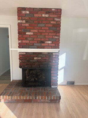 Una llar de pedra amb mantell blanc, situada en una habitació amb terra de fusta i una porta blanca.