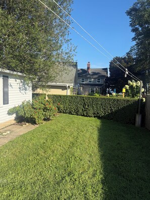 A residential backyard with a well-maintained lawn, a hedge, and a house with a chimney. - Adorable 2-bedroom Seasonal Rental in Milford Beach Neighborhood (Milford)
